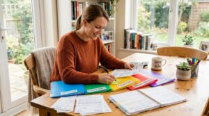 Método Kakebo: o que é, como funciona e como aplicar no seu dia a dia 3 Uma pessoa sentada à mesa organizando documentos financeiros em categorias com pastas coloridas e anotações, representando o planejamento mensal de ga